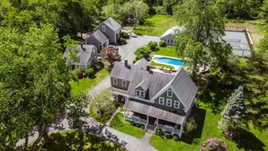 Une grande maison avec une piscine, entourée d’une végétation luxuriante et d’arbres.