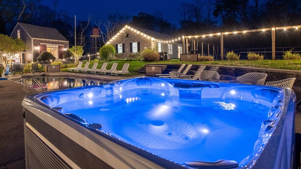 Un bain à remous avec une piscine, des chaises longues et une maison décorée de guirlandes lumineuses.