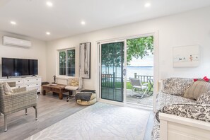 A spacious living room with a large flat-screen TV, comfortable seating, and a view of the water through glass doors. - Cozy Cottage with all the amenities on  Lake Ontario (Bath)