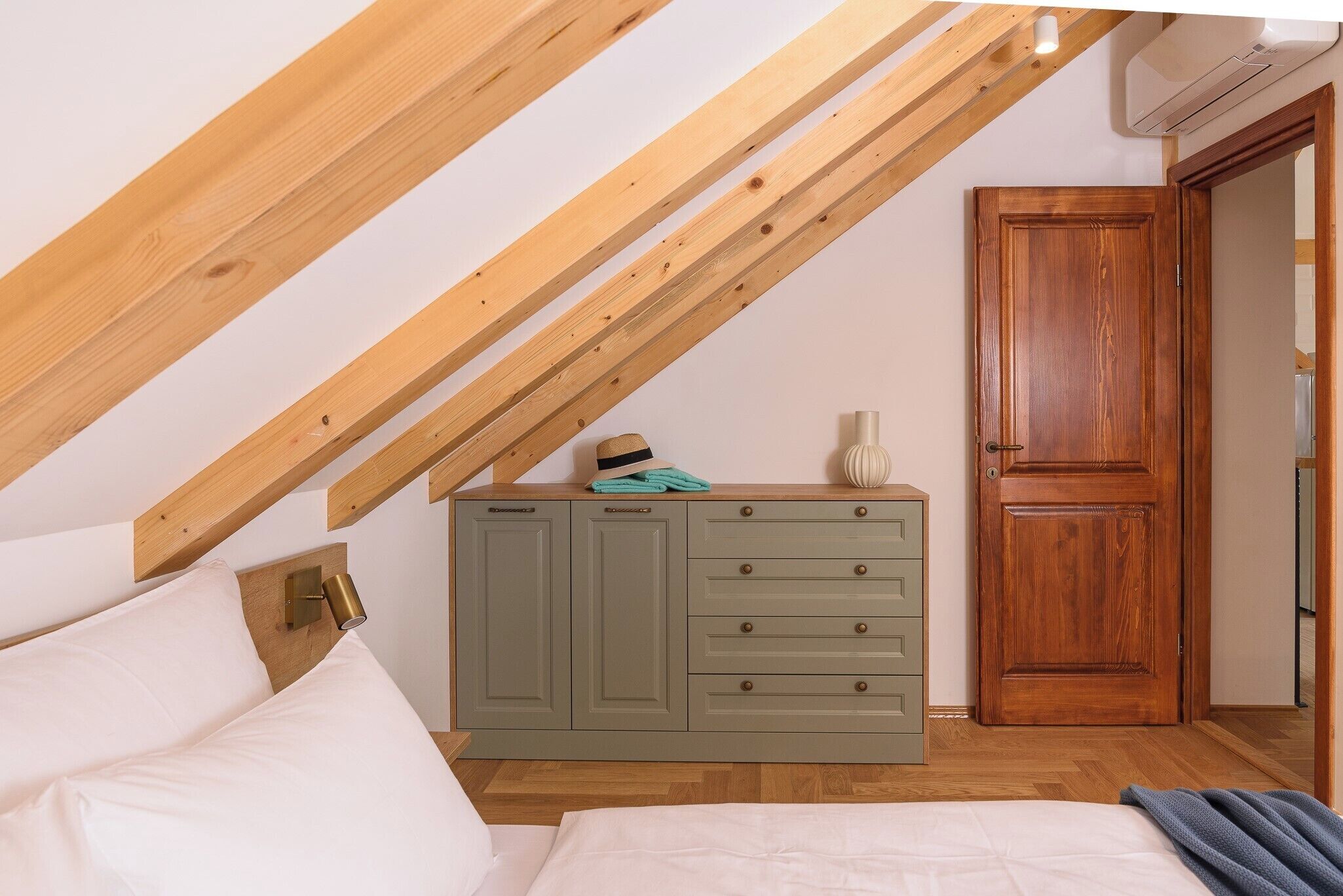 Un dormitorio con techo inclinado, un armario de madera, una puerta y una cama.