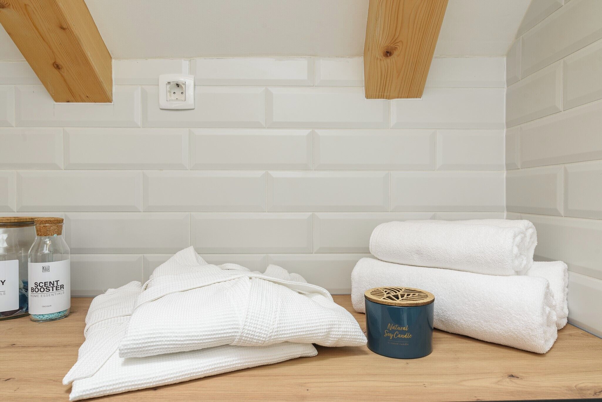 A bathroom with white subway tiles, wooden beams, a white towel, a candle, and two bottles of essential oils.