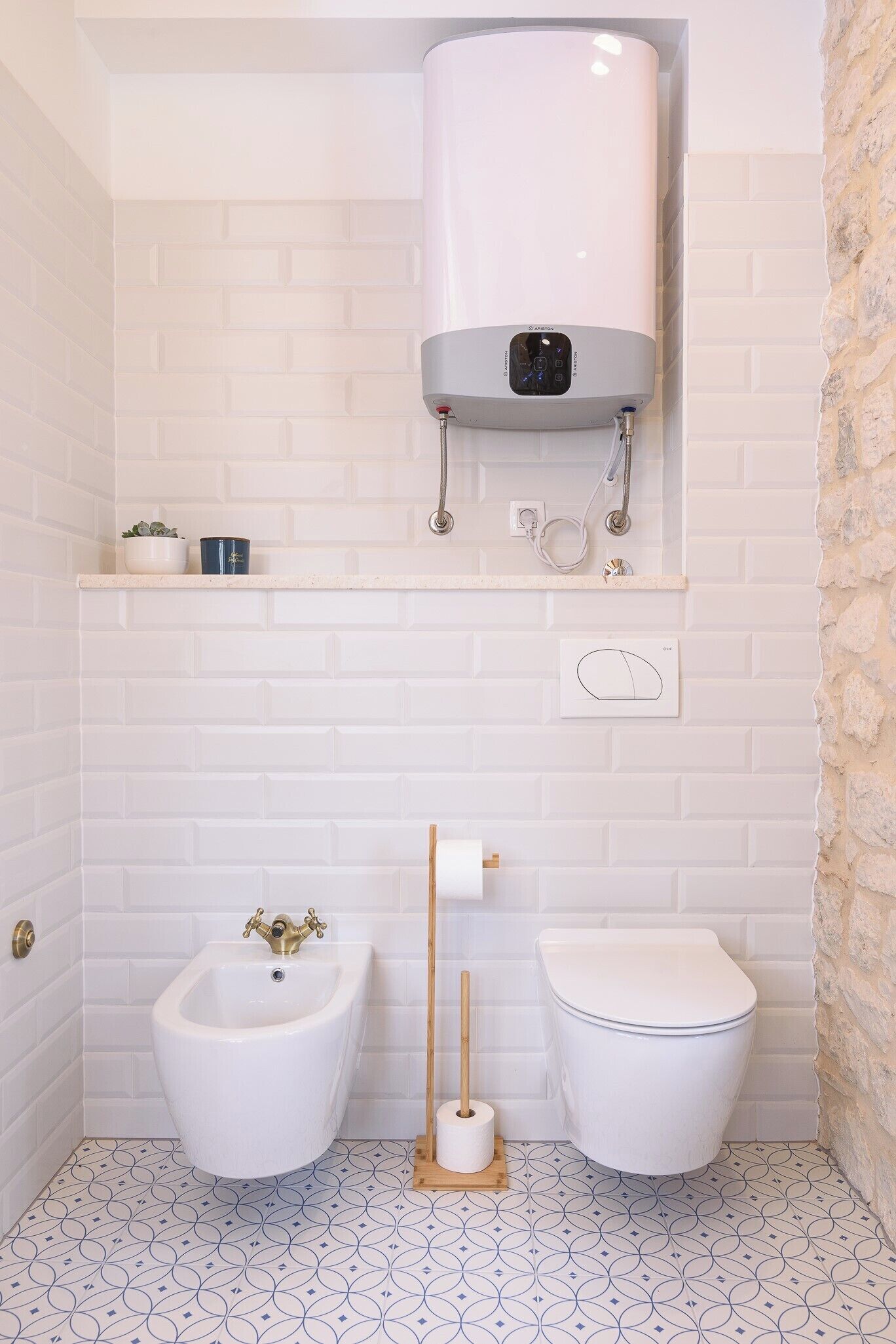 Un baño con inodoro blanco, bidé y calentador de agua instalado en la pared.