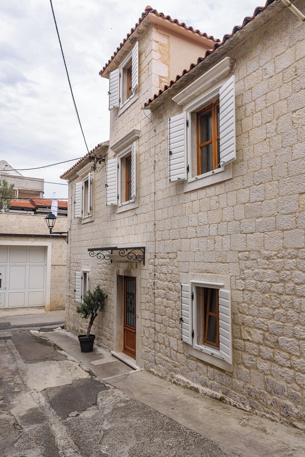 A stone building with a central entrance, multiple windows with shutters, and a small potted plant. - Oleander Center Suites (Trogir)