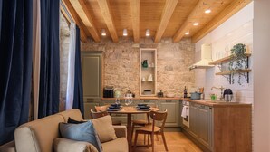 A cozy living room with a sofa and chairs, a wooden dining table, and a kitchen with stone walls and wooden beams. - Oleander Center Suites (Trogir)