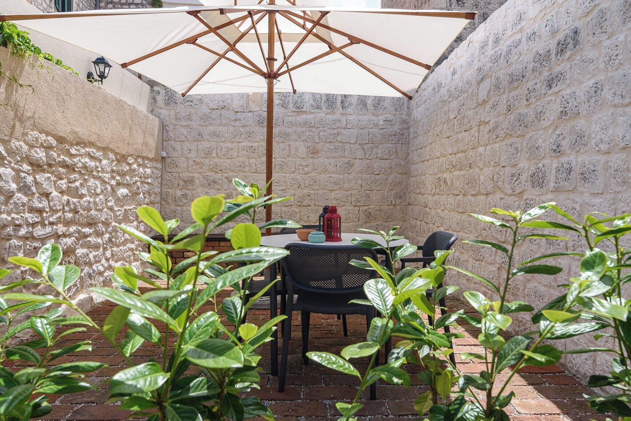 Un patio con mesa y sillas, un paraguas grande y plantas en macetas.