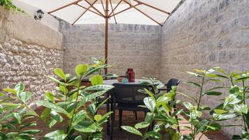Un patio con mesa y sillas, un paraguas grande y plantas en macetas.