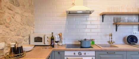 A kitchen with a stone wall, white tiled backsplash, a stove, oven, and a sink.