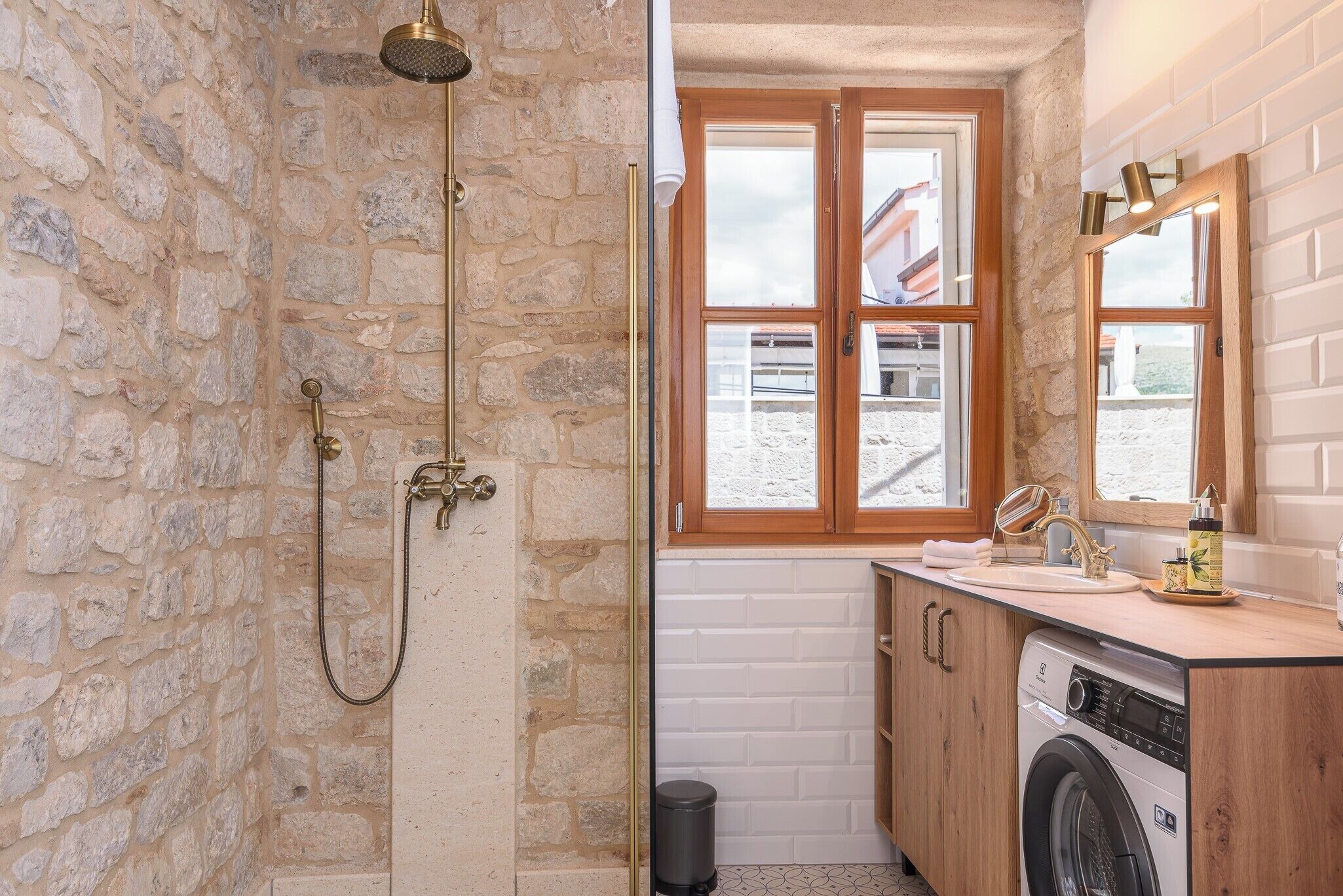 Ein Badezimmer mit Steinwand, Holzfenster, Waschbecken, Waschmaschine und Dusche.