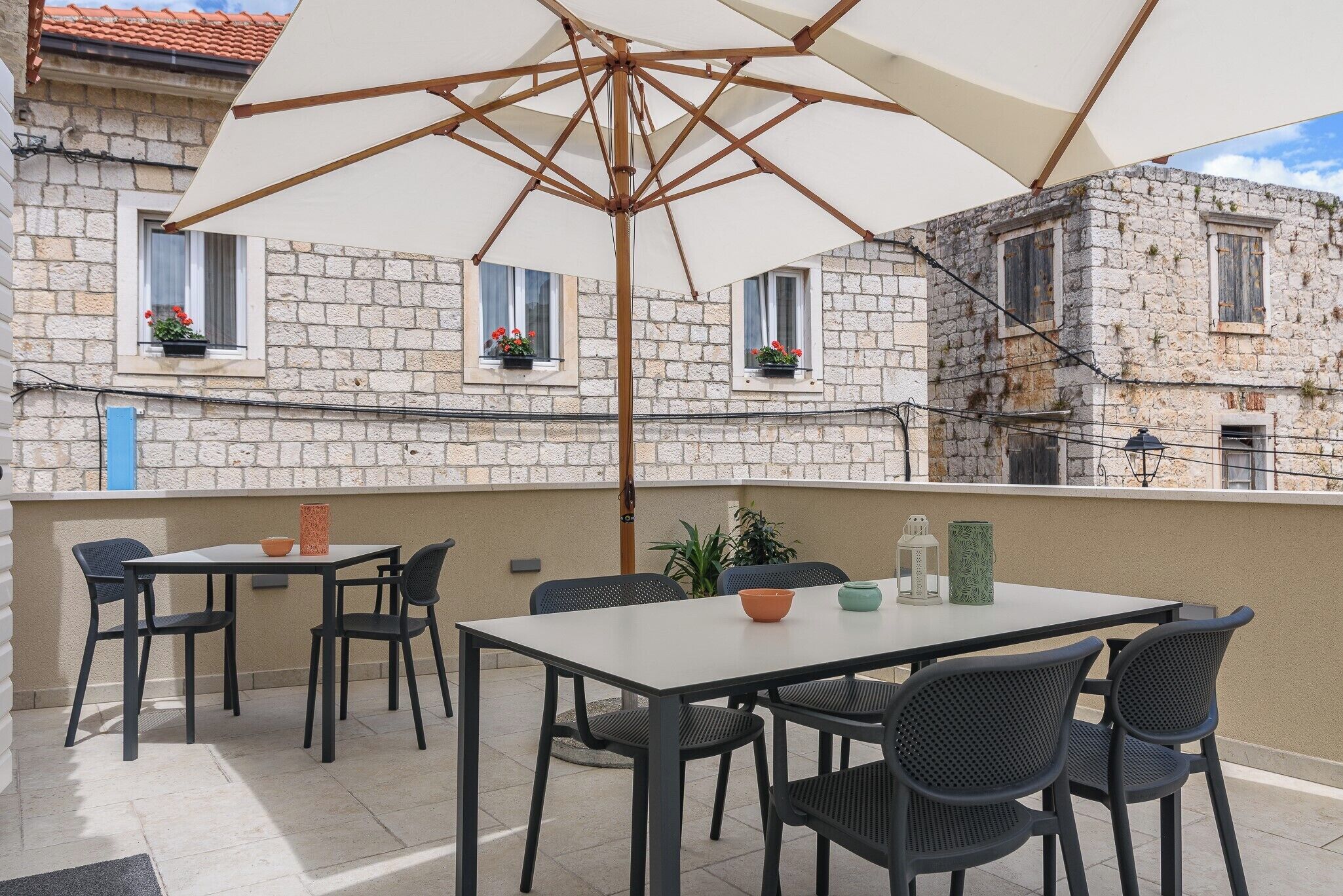 An outdoor patio with a table and chairs, an umbrella, and a view of stone buildings.