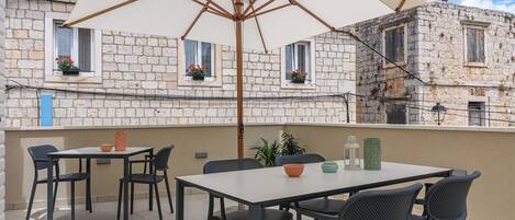 An outdoor patio with a table and chairs, an umbrella, and a view of stone buildings.