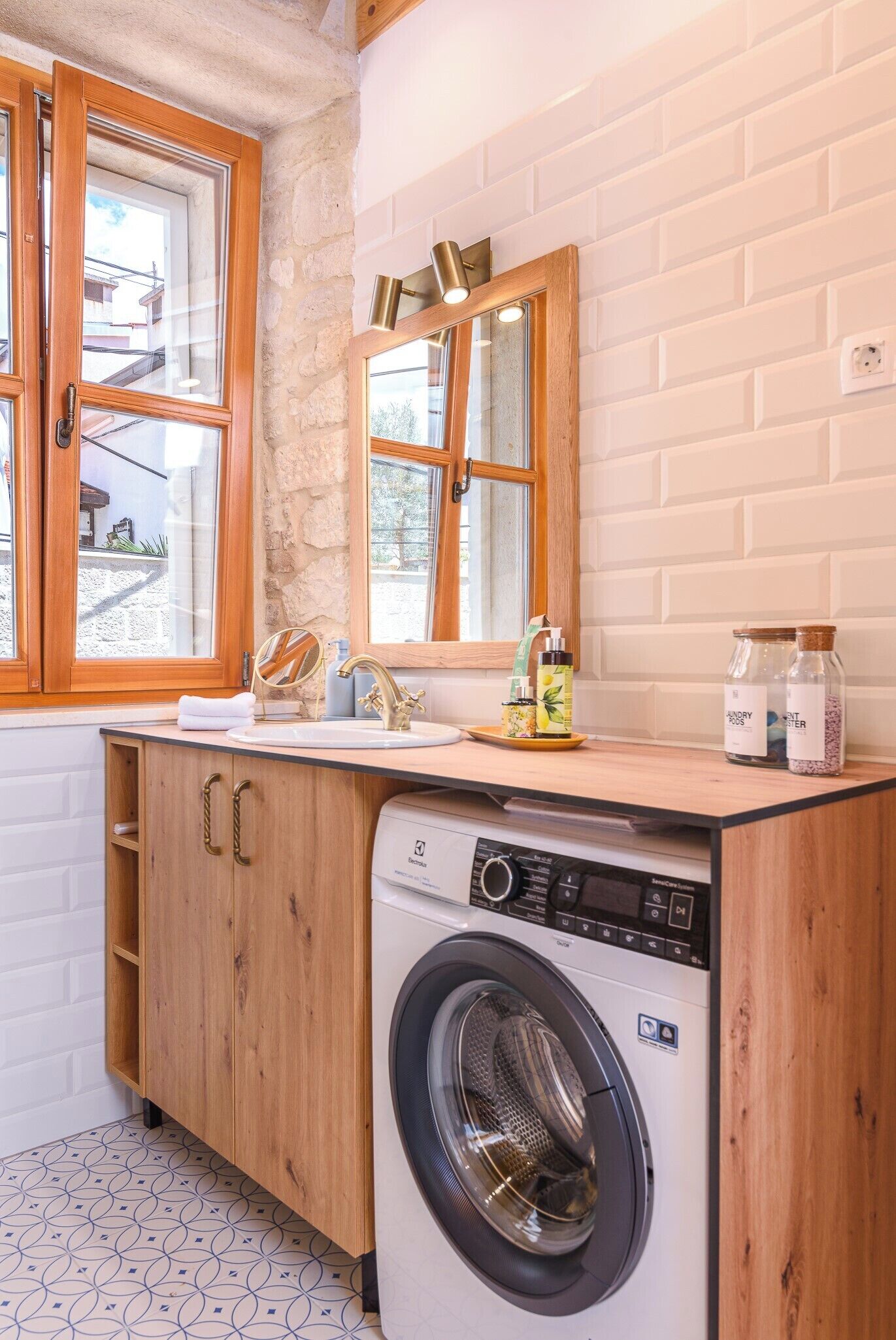 A compact laundry room with a washing machine, wooden cabinets, a sink, and a window with a view of the outside.