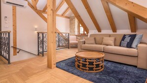 A loft-style room with exposed wooden beams, a beige sofa, a round wooden coffee table, and a blue rug. - Oleander Center Suites (Trogir)