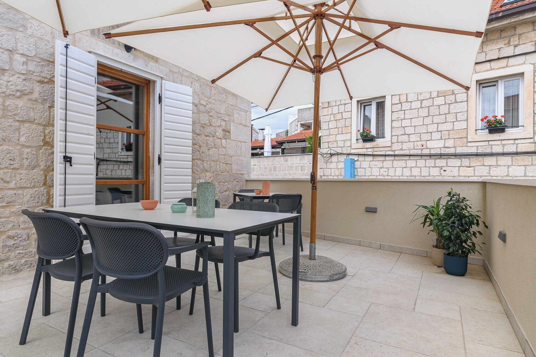 An outdoor patio with a table and chairs, a large umbrella, and a potted plant.