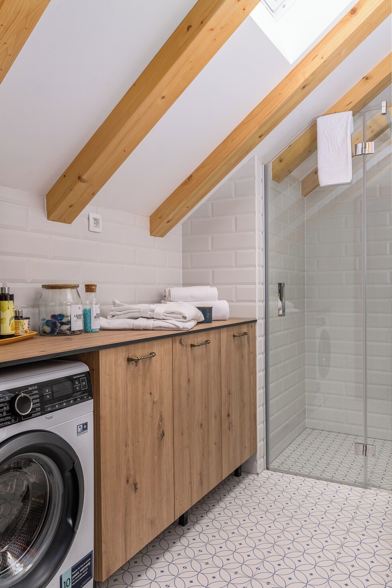 A modern kitchen with wooden beams, a washing machine, and a glass shower enclosure.
