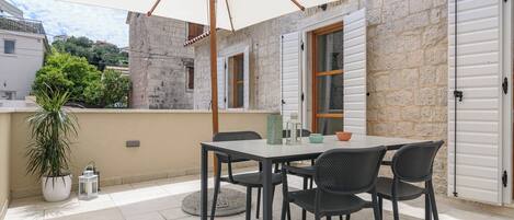 En udendørs terrasse med et bord, stole, en stor parasol og en potteplante.