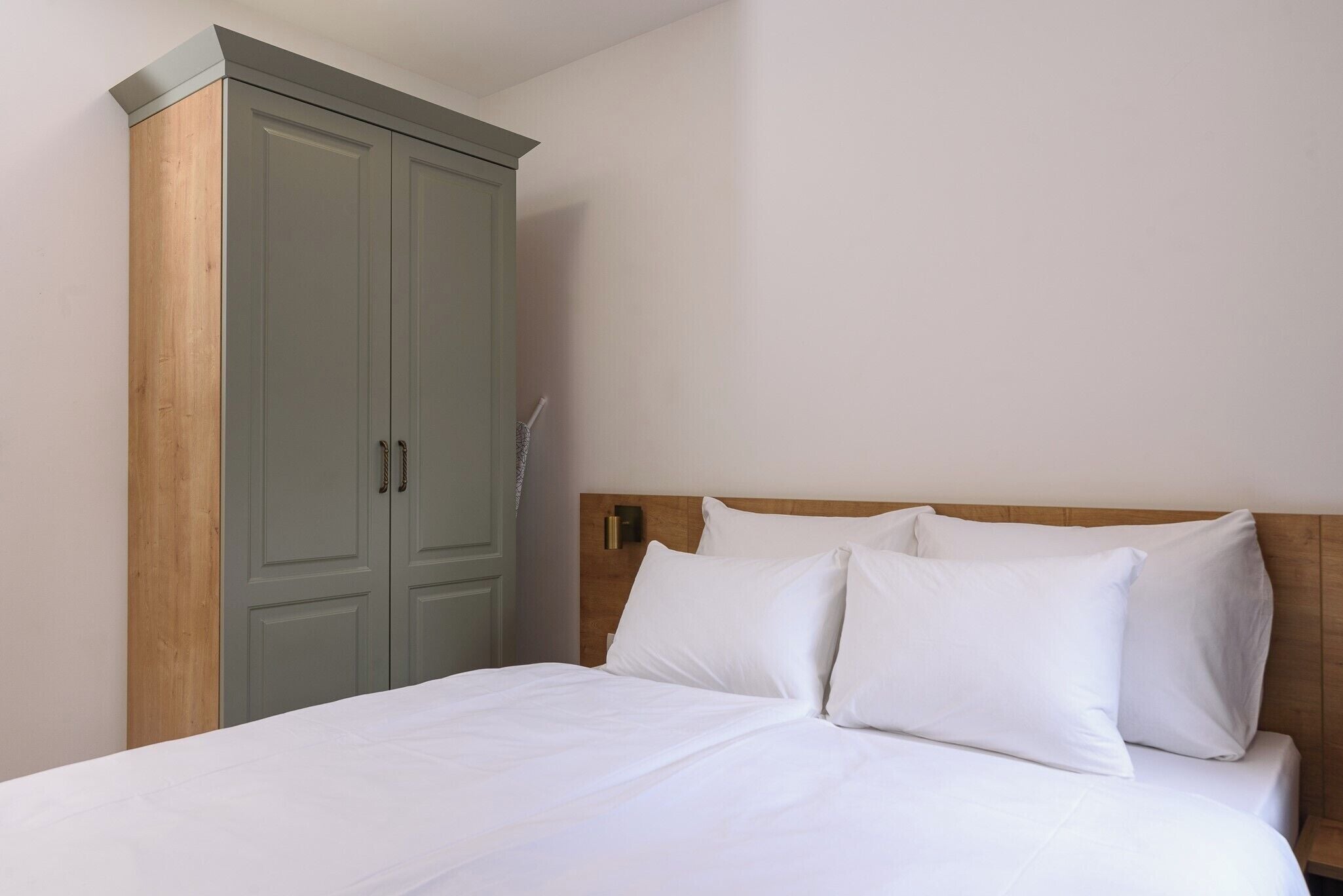 A bedroom with a bed, white bedding, a wooden headboard, and a green wardrobe.