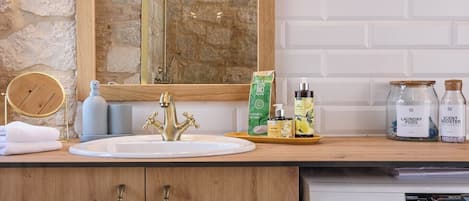 Un baño con tocador de madera, lavamanos, espejo, ducha y lavadora.
