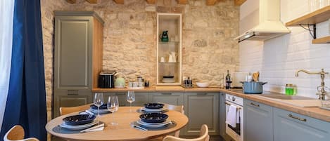 A cozy kitchen with a stone wall, wooden ceiling, and a round dining table with chairs.
