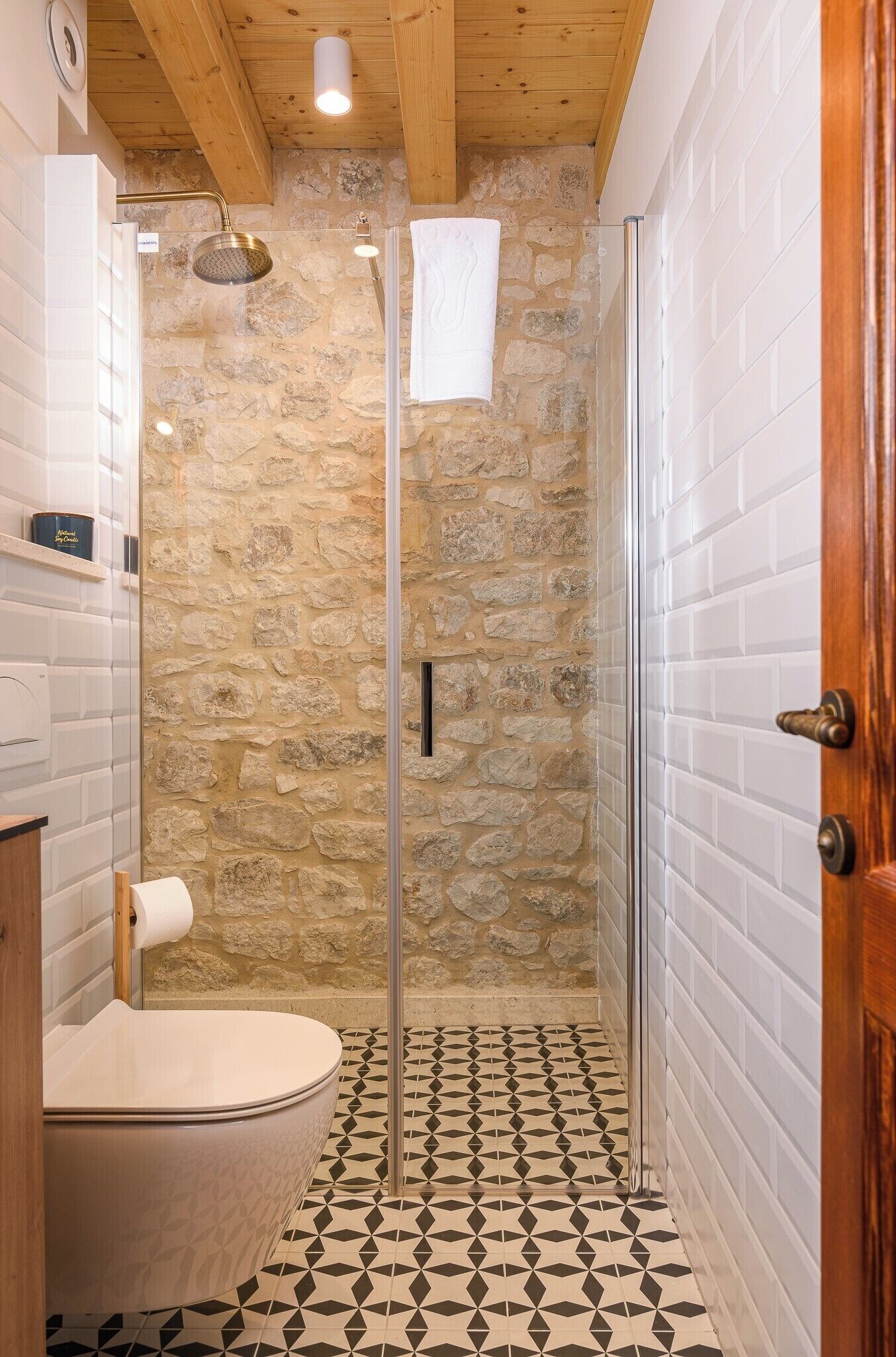 A bathroom with a stone wall, a shower, a toilet, and a patterned floor.