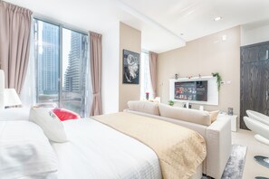 Habitación de hotel moderna con una cama grande, un sofá, un televisor y vistas a edificios altos.