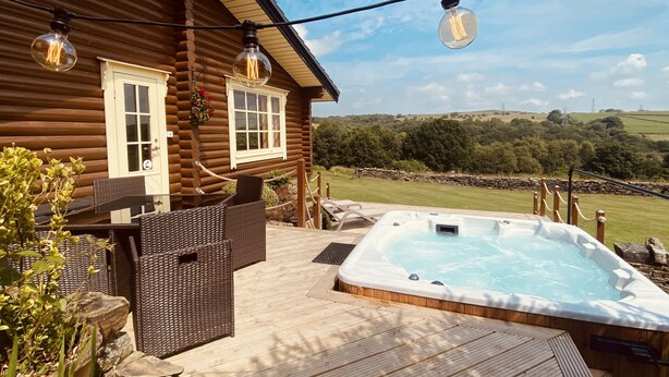 Una cabaña de madera con jacuzzi, muebles de mimbre y vistas al campo.