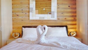 Una cama bien hecha con un arreglo de toallas con forma de corazón, un cabecero de madera y un adorno geométrico en la pared.