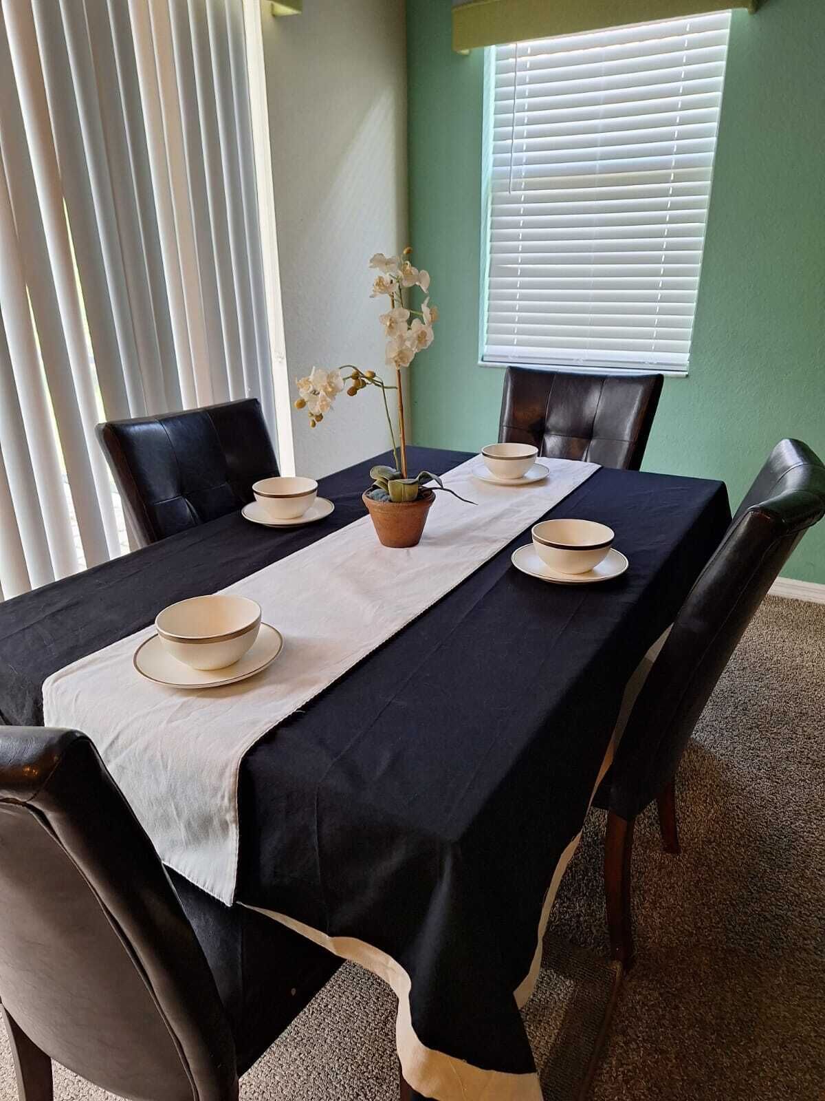 A dining table set with white plates and bowls, a potted orchid, and a white table runner.