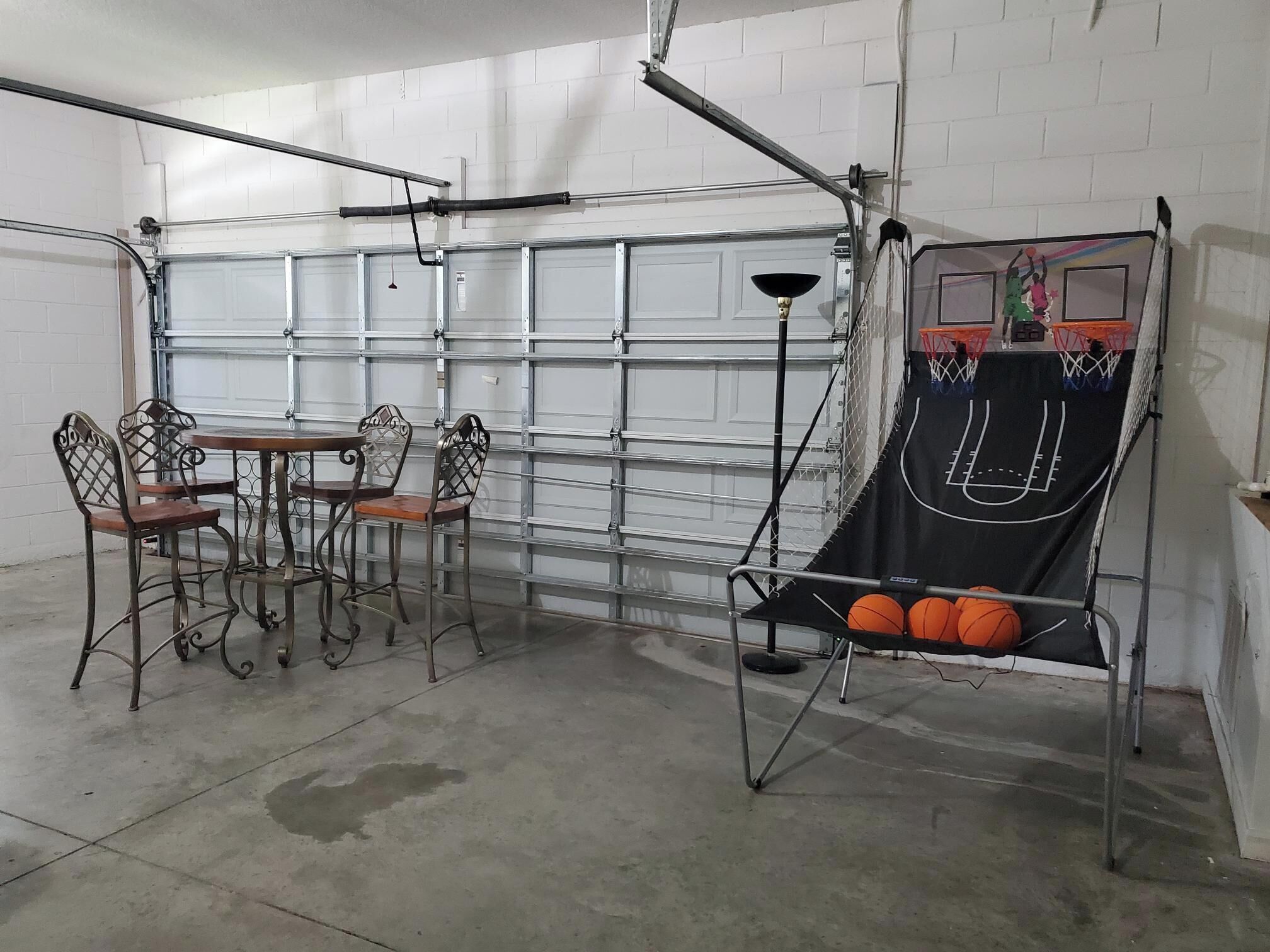 Un garaje con aro de baloncesto, una mesa de comedor con sillas y una lámpara de pie.
