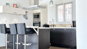 Une cuisine moderne dotée d’un îlot central, de tabourets de bar, d’un four encastré et d’une fenêtre avec des stores.