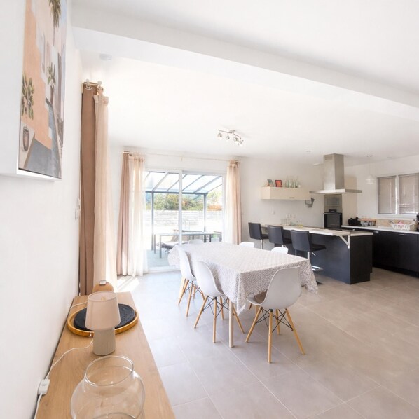 Un espace repas moderne avec une table et des chaises, une cuisine en arrière-plan et une vue à travers une porte vitrée.