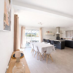 Un comedor moderno con una mesa y sillas, una cocina al fondo y vistas a través de un ventanal.