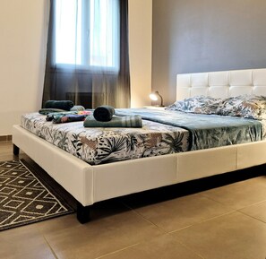 A neatly made bed with patterned bedding, a bedside lamp, and a window with curtains. - Villa Avec Piscine au Coeur D'une Station Balnéaire (La Seyne-sur-Mer)
