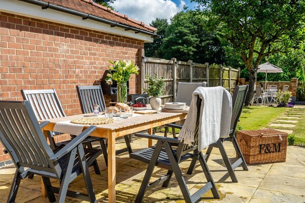 A patio with a wooden table, chairs, and a basket labeled "F&M". - The Birdie- Sleeps 5 guests (York)