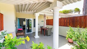 A covered patio area with a table and chairs, a potted plant, and a sliding glass door leading to an indoor space. - Luxury Studio, Oasis of Peace, Centrally Located Close to Most Beautiful Beaches (Sint Willibrordus)