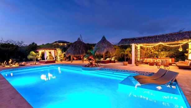 A swimming pool with lounge chairs, a thatched-roof structure, and string lights. - Luxury Studio, Oasis of Peace, Centrally Located Close to Most Beautiful Beaches (Sint Willibrordus)