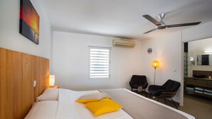 A hotel room with a bed, a ceiling fan, an air conditioning unit, a window with blinds, a desk with a chair, and a bathroom visible through an open door. - Luxury Studio, Oasis of Peace, Centrally Located Close to Most Beautiful Beaches (Sint Willibrordus)