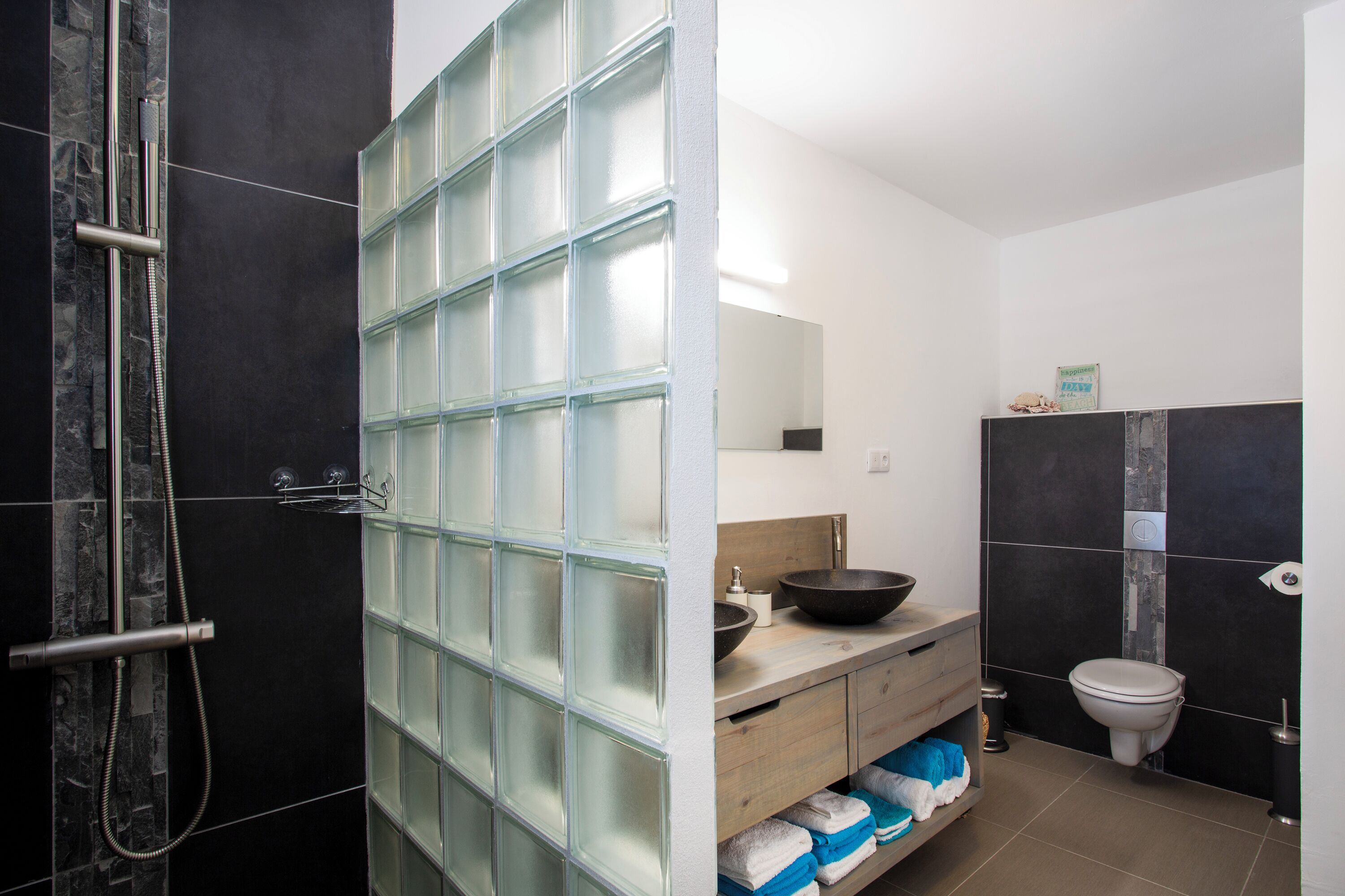 A modern bathroom with a glass shower enclosure, a wooden vanity with a bowl sink, and a toilet.