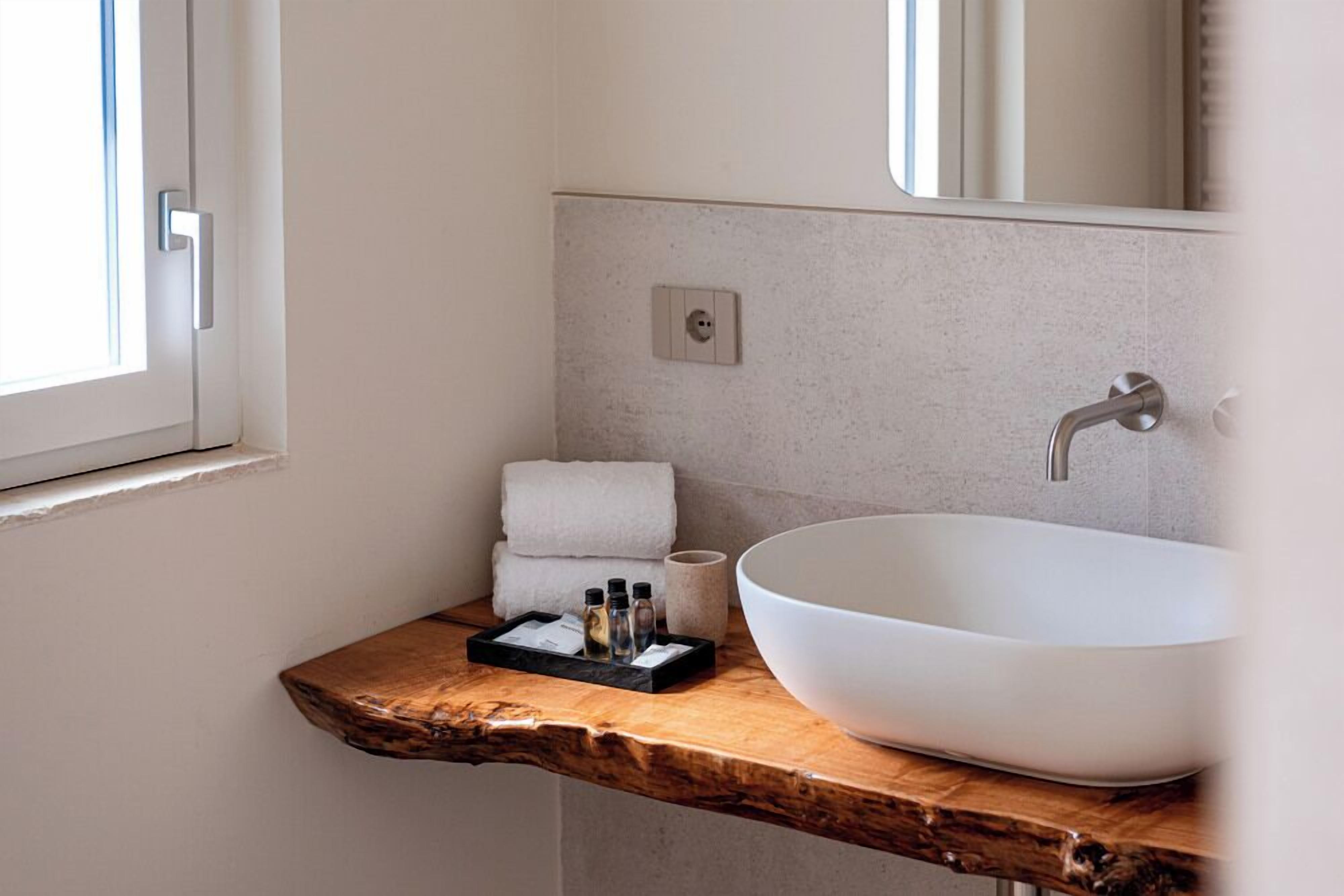 A bathroom with a large white sink, a wooden countertop, a towel rack with folded towels, and a mirror above the sink.