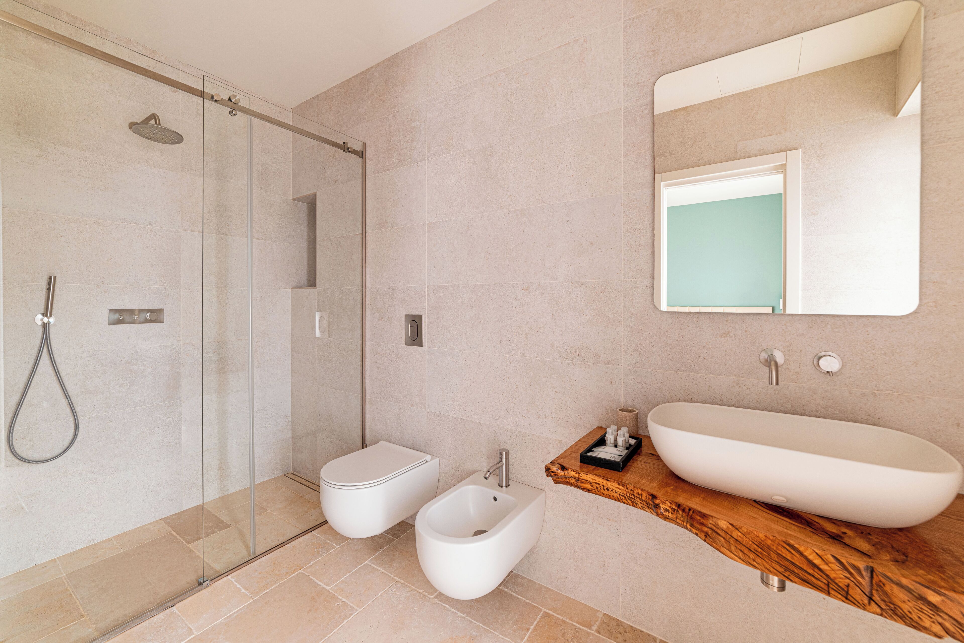 A modern bathroom with a glass-enclosed shower, a bidet, a freestanding bathtub, and a wooden vanity.