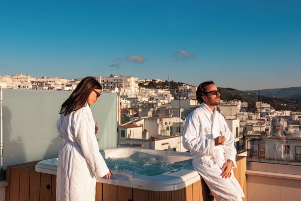 Two people in white bathrobes sitting by a hot tub with a cityscape view in the background. - DIMORA GARIBALDI (Peschici)