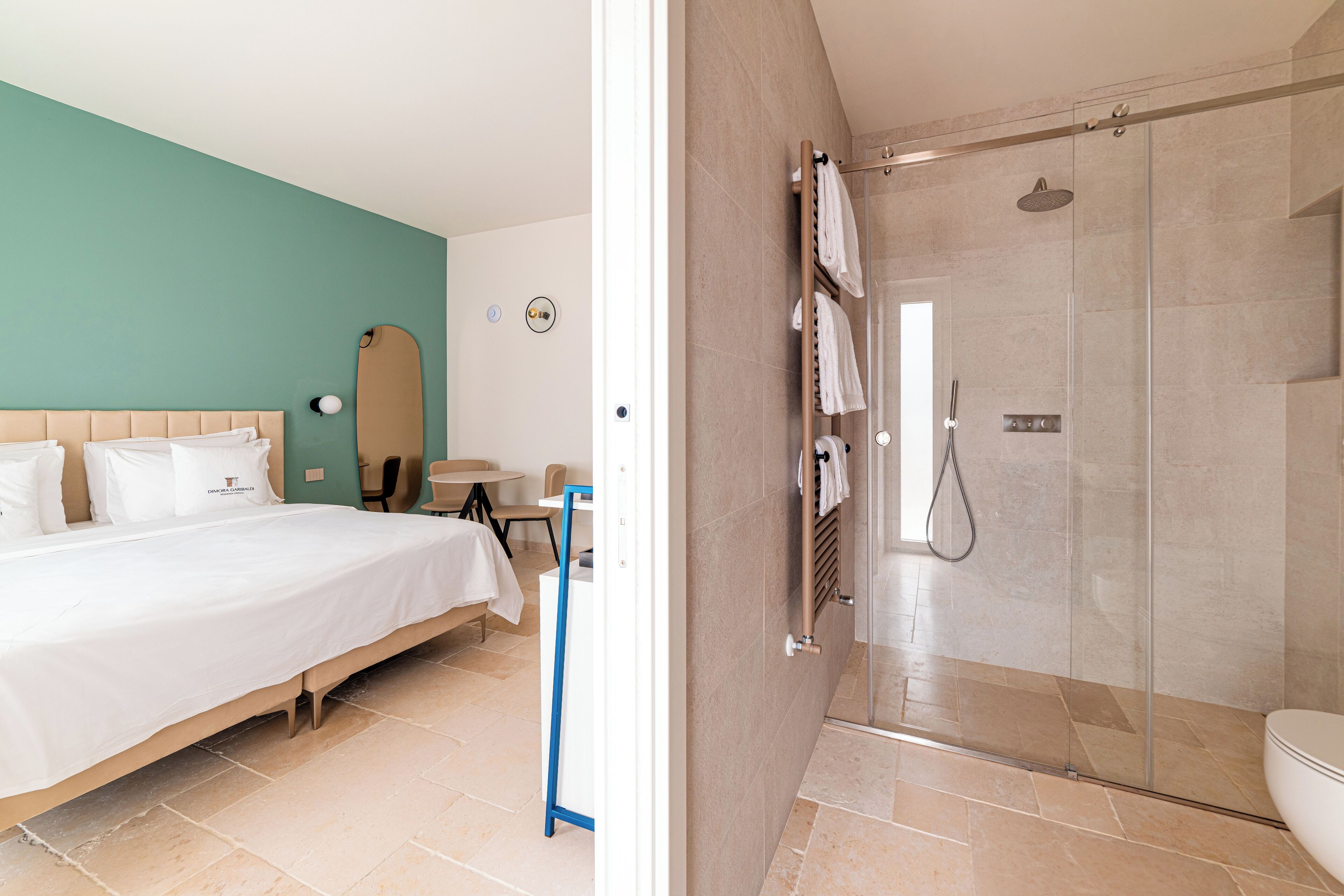 Hotelkamer met een bed, een tafeltje, een stoel, een douchecabine met glazen deuren en een toilet.