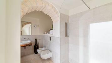 Un baño moderno con un arco de piedra, un lavamanos blanco, un bidé y una zona de ducha.