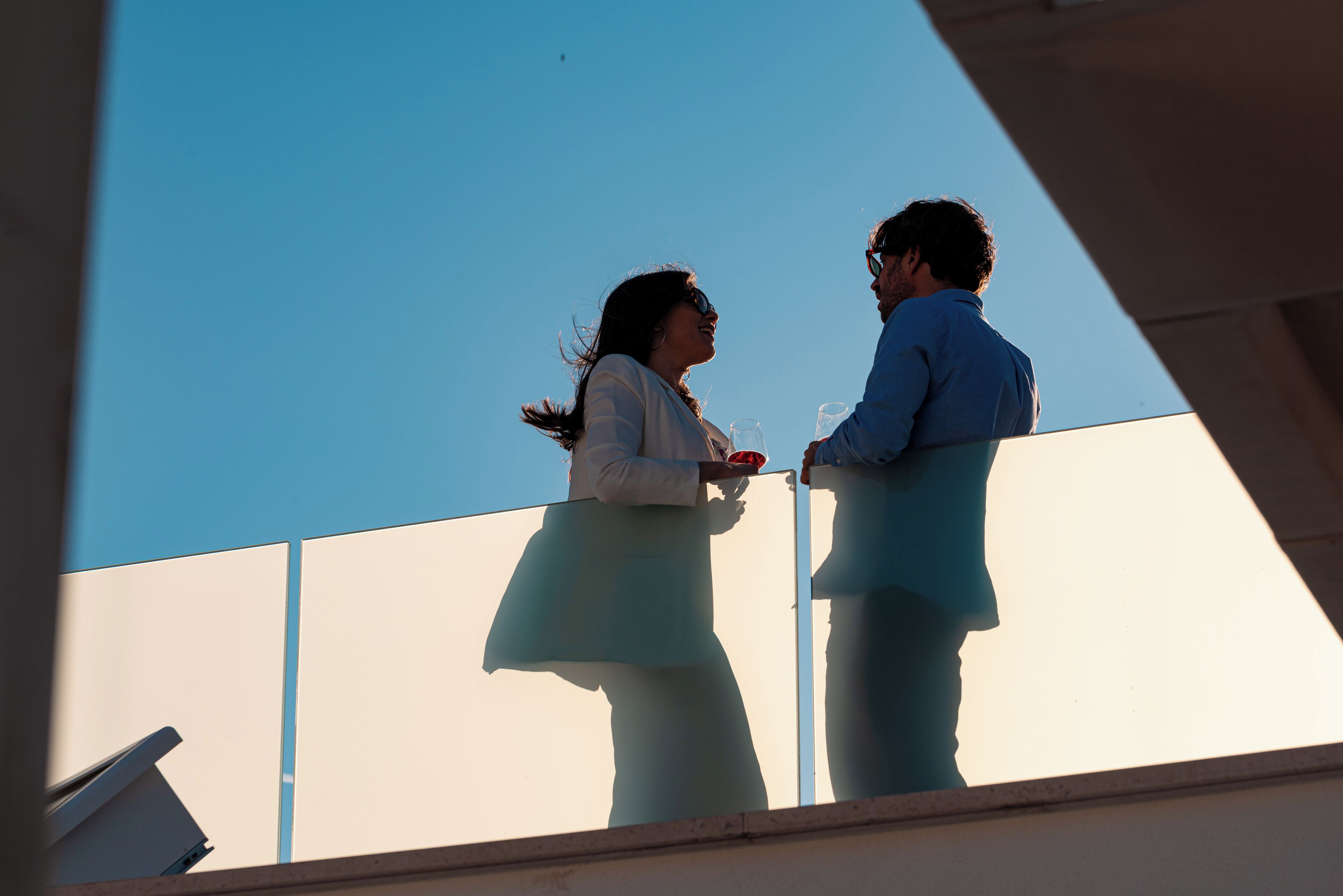 Two people standing on a balcony with a clear sky in the background.