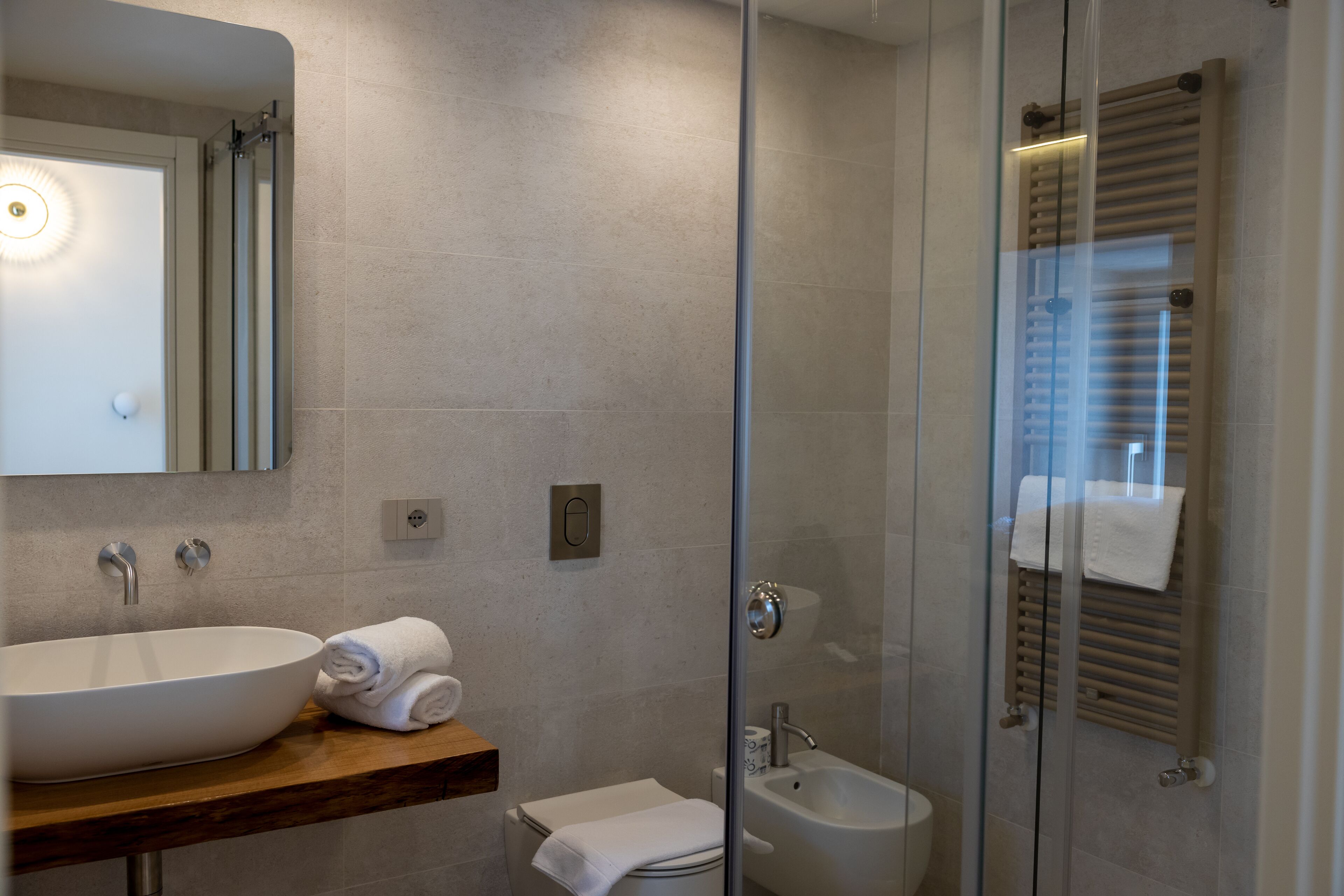 A modern bathroom with a large vessel sink, a glass-enclosed shower, and a wooden vanity.