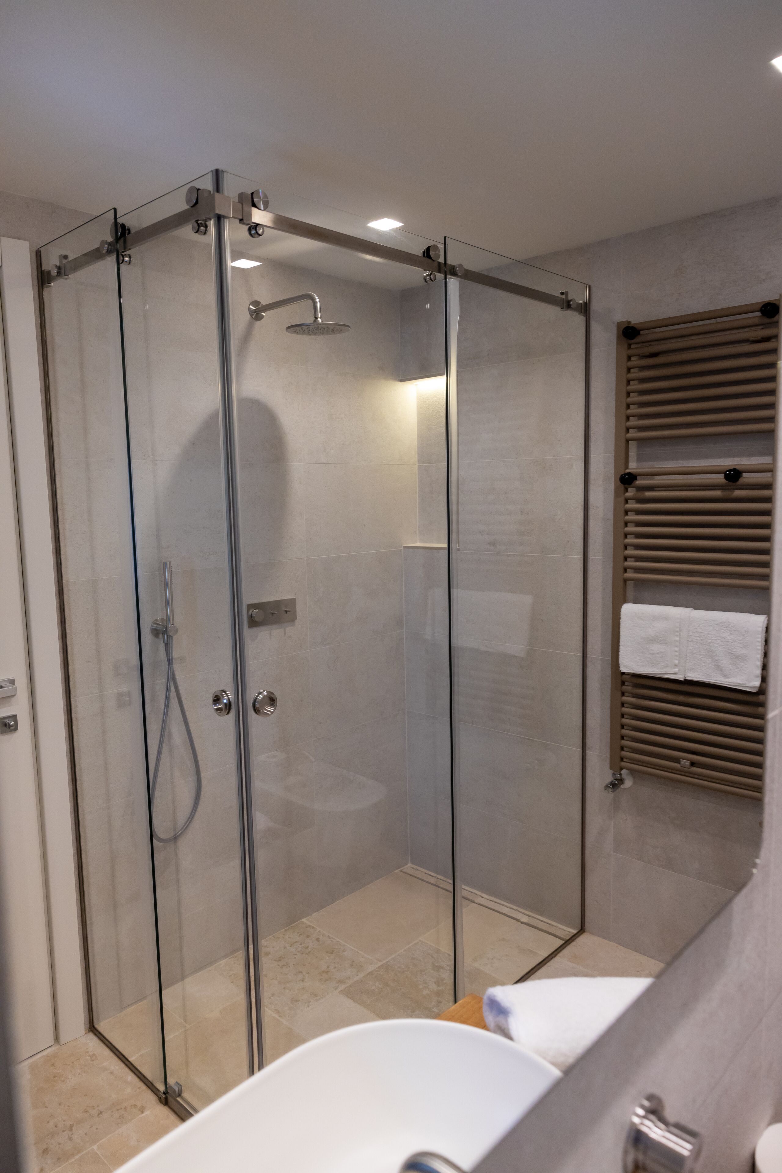 A modern bathroom with a glass-enclosed shower, a white bathtub, and a towel rack with towels.