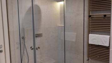 A modern bathroom with a glass-enclosed shower, a white bathtub, and a towel rack with towels.