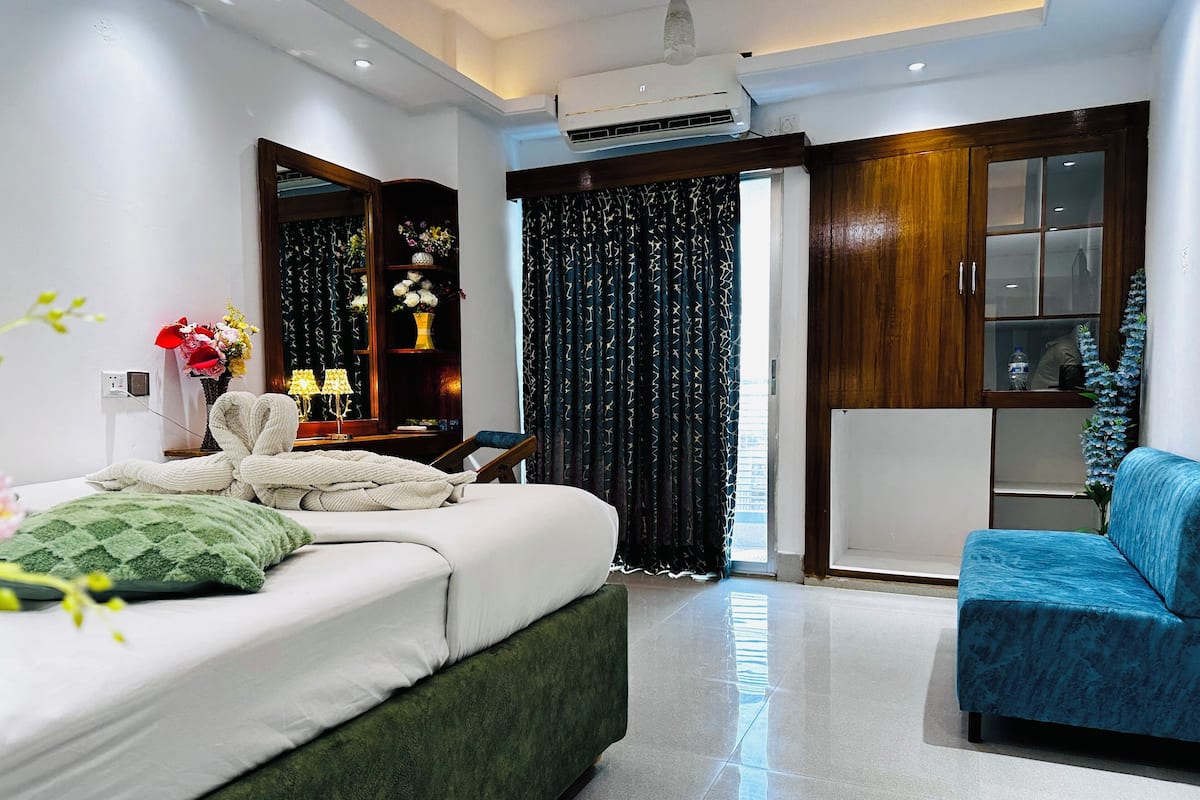 Un dormitorio moderno con una cama, un sillón azul, un armario de madera y una ventana con cortinas.