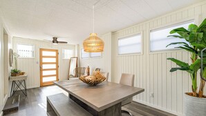 Un comedor moderno con una mesa de madera, asientos tipo banco, una lámpara colgante tejida y una planta en maceta.