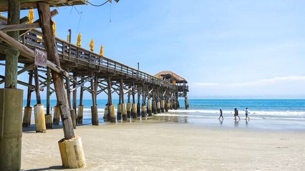Un muelle de madera que se adentra en el océano, con una estructura de techo de paja al final.