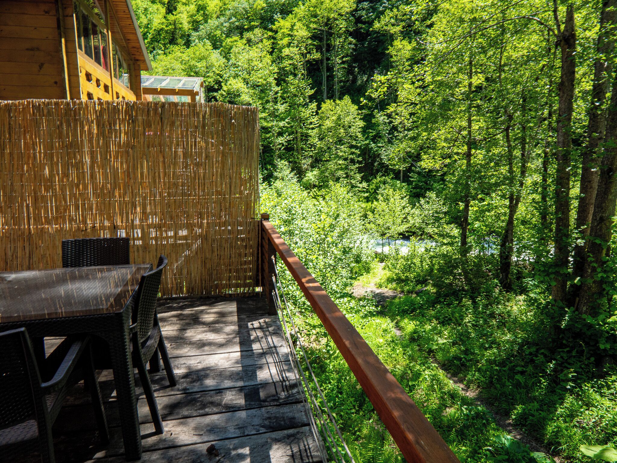 A wooden deck with a table and chairs, overlooking a dense forest and a river.